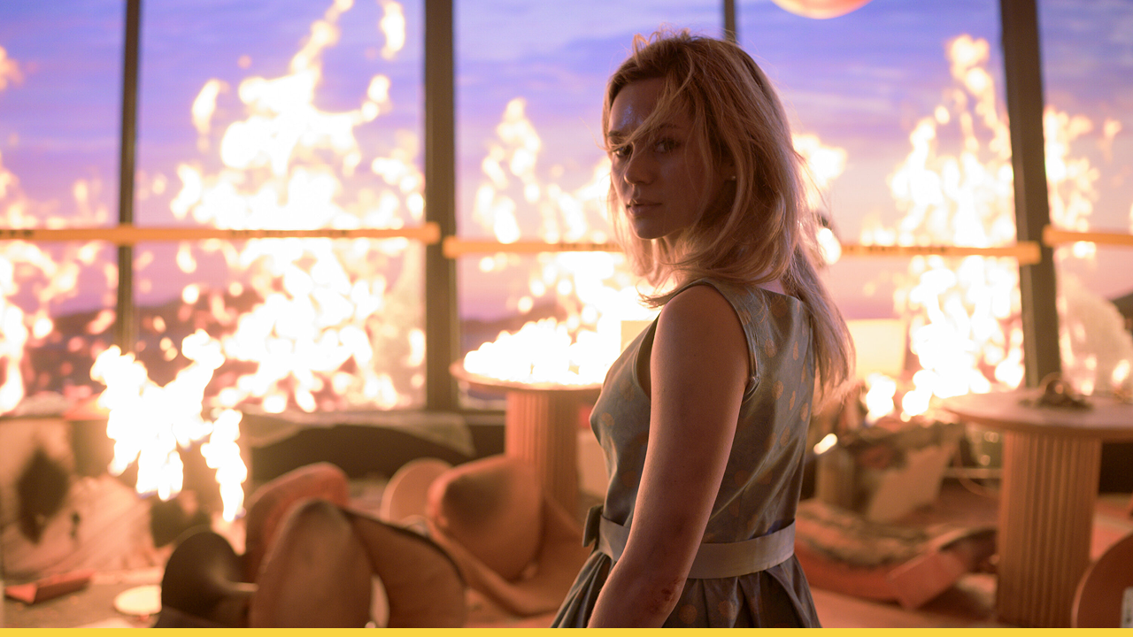 A woman stands amidst chaos as flames engulf a high-rise restaurant in a tense moment from Final Destination: Bloodlines