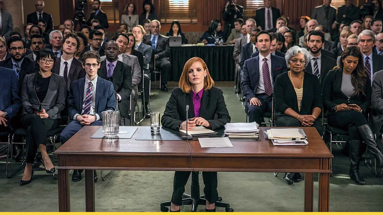 Jessica Chastain as a powerful lobbyist testifying before a congressional committee in Miss Sloane, surrounded by a packed courtroom