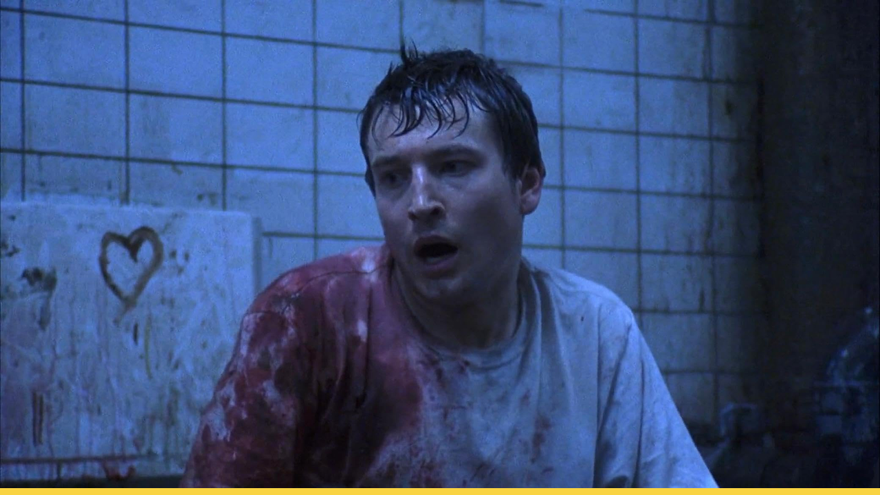 A blood-soaked man gasps for breath in a grimy bathroom in a chilling scene from Saw
