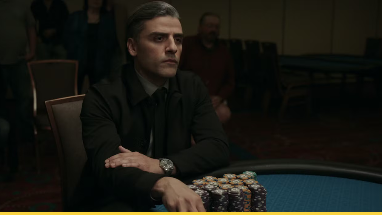 Oscar Isaac sits at a poker table in The Card Counter, calmly focused with stacks of chips in front of him in a dimly lit casino room