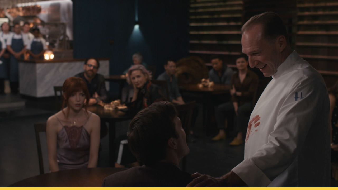 A sinister chef addresses uneasy diners in a high-end restaurant with unsettling intentions