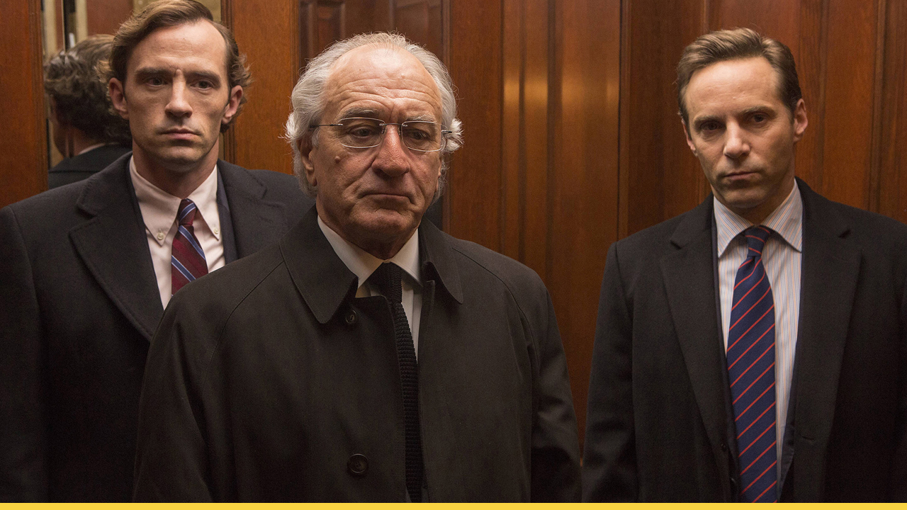 Robert De Niro as Bernie Madoff stands in an elevator with two men in a scene from The Wizard of Lies, portraying the fallout of one of the biggest financial frauds in U.S. history