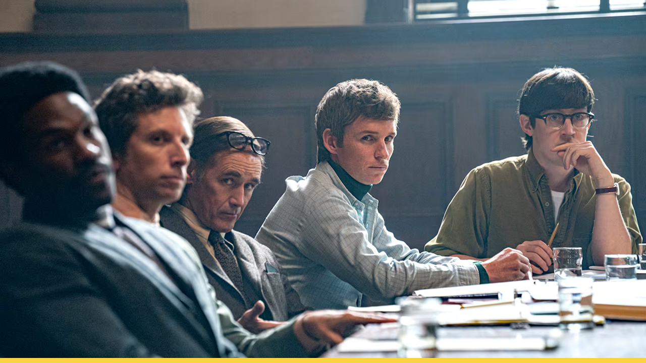 Eddie Redmayne and fellow cast members sit in a tense courtroom setting in The Trial of the Chicago 7, portraying the high-profile political trial following the 1968 Democratic National Convention protests
