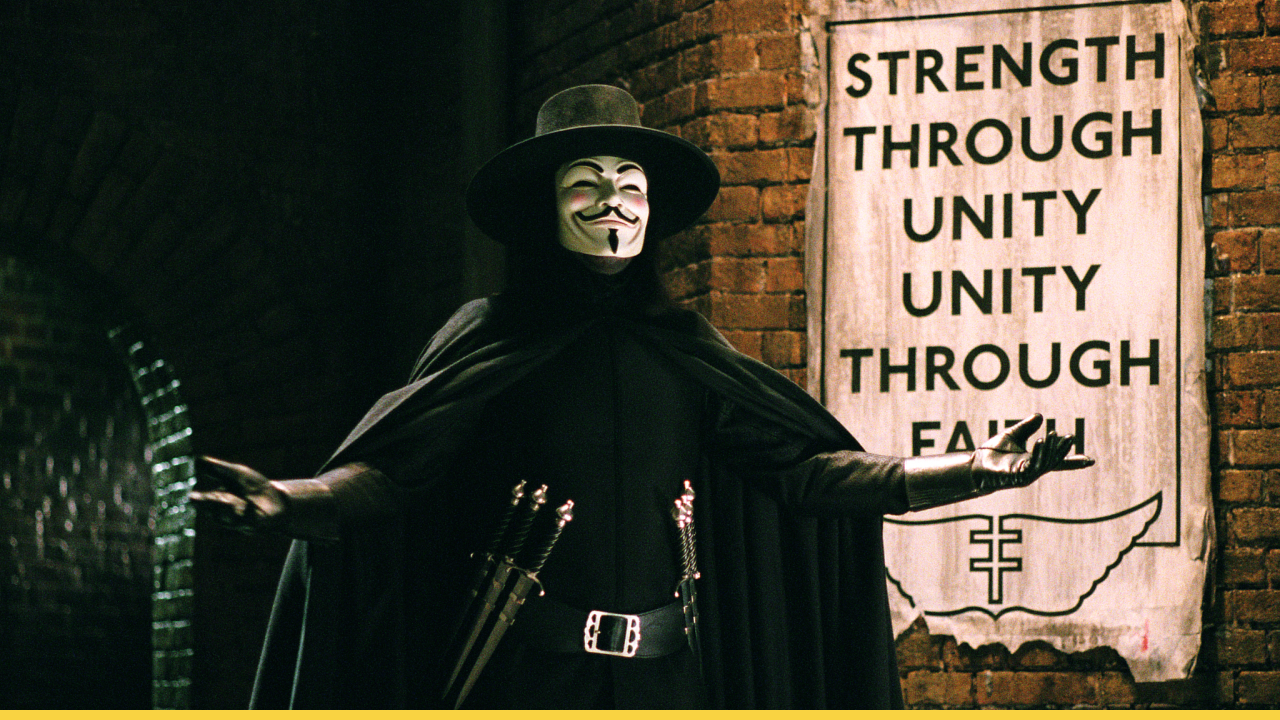 A masked V from V for Vendetta stands defiantly before a propaganda poster reading “Strength Through Unity, Unity Through Faith” in a dystopian London