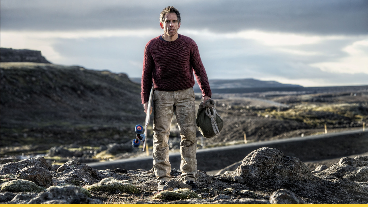 A man stands alone on rocky terrain holding a skateboard and a bag, surrounded by mountains and dramatic skies.